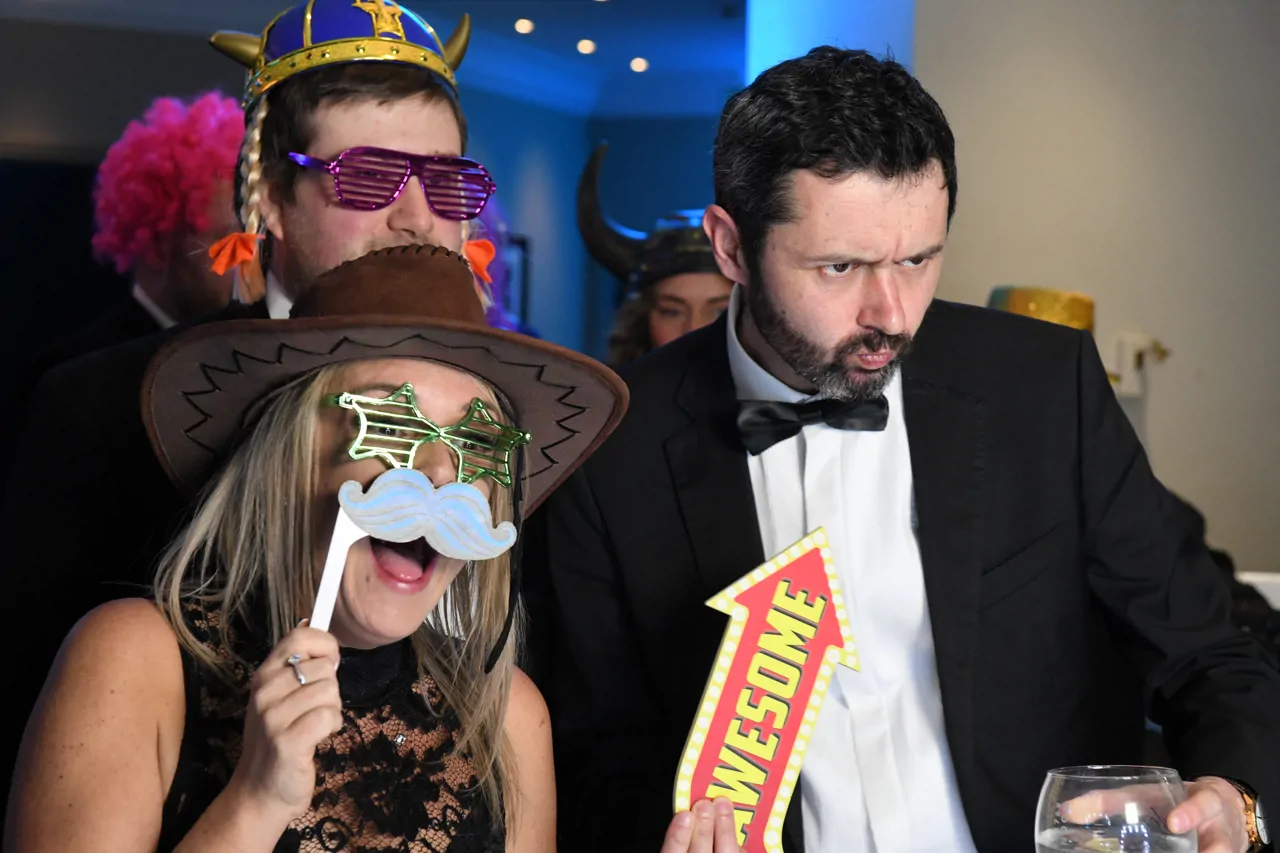 Group of colleagues in formal wear holding up fancy dress props