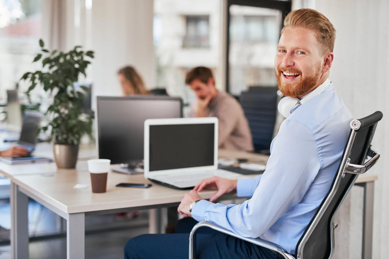 A man smiling sat at his laptop in an office