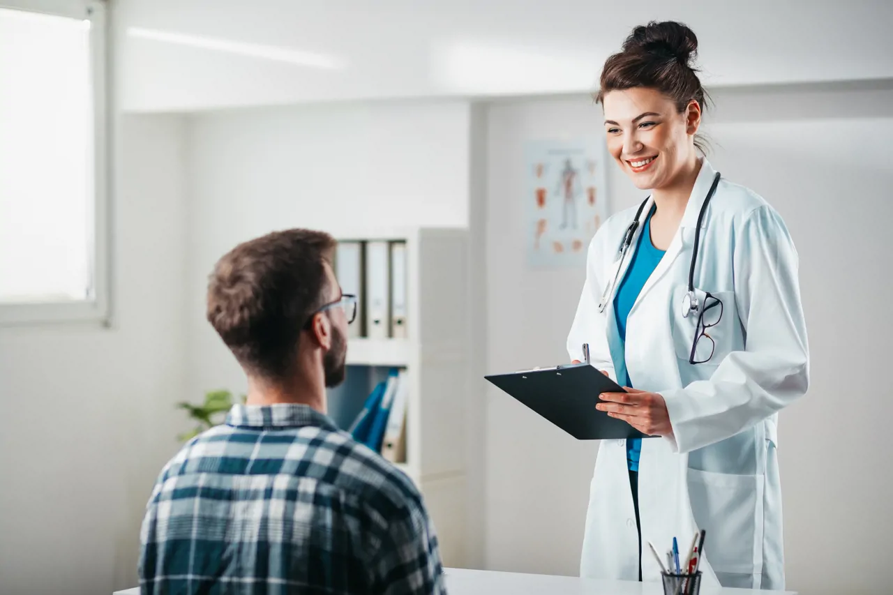 Patient sat listening to doctor holding clipboard in doctors office