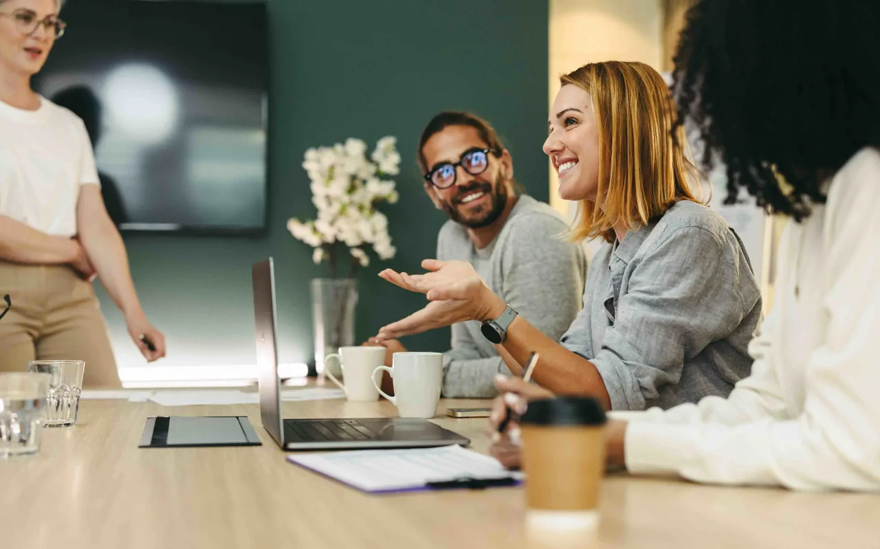 Four professionals smiling in a meeting room with laptop and flowers